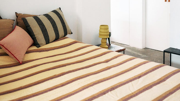 striped duvet, pink and brown and black striped pillow in a room with white walls and a yellow table lamp