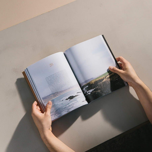 Open book with scenic images held by hands on a neutral surface