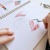 Person drawing American flags in a notebook with a paintbrush.