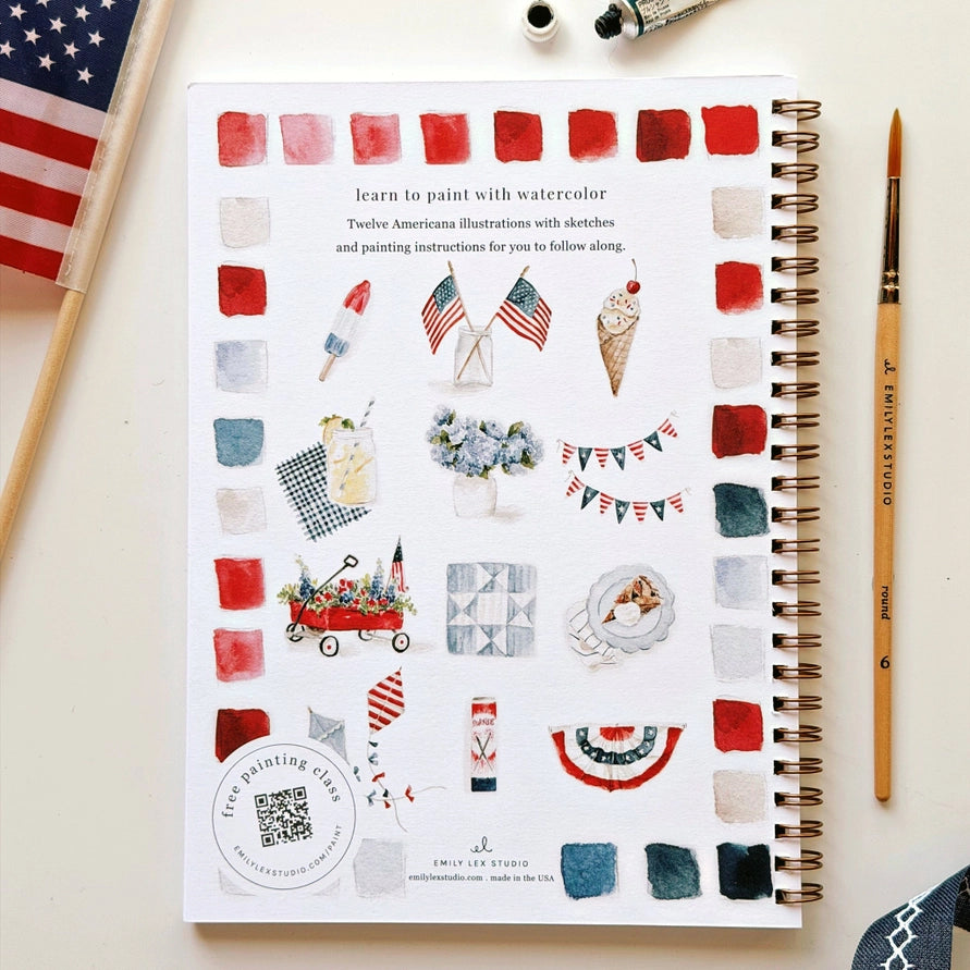 Notebook cover with watercolor illustrations and American flag, surrounded by art supplies.
