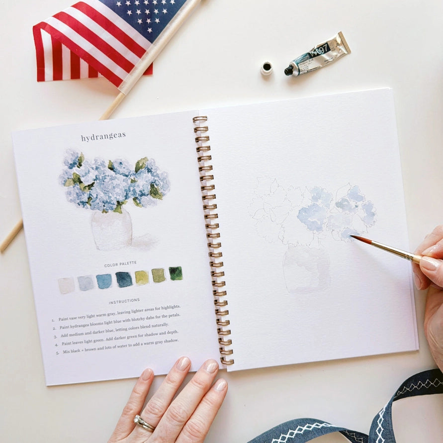 Open book with watercolor painting and color palette on a white surface