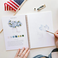 Open book with watercolor painting and color palette on a white surface