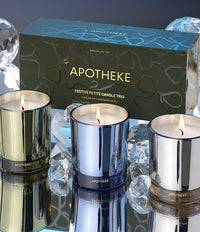 Three lit candles in metallic holders with a 'Apotheke' box in the background.