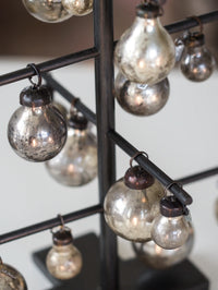 Decorative hanging lights with glass bulbs on a metal stand against a neutral background