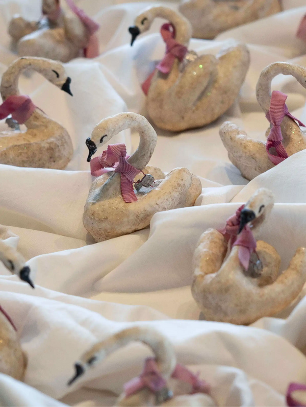 Decorative swan figurines with pink bows on a white surface