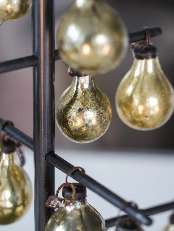 Vintage-style Christmas bulbs hanging from a black metal frame against a neutral background