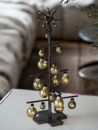 Decorative metal tree with hanging gold bulb ornaments on a blurred background