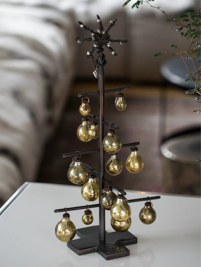 Decorative metal tree with hanging gold bulb ornaments on a blurred background