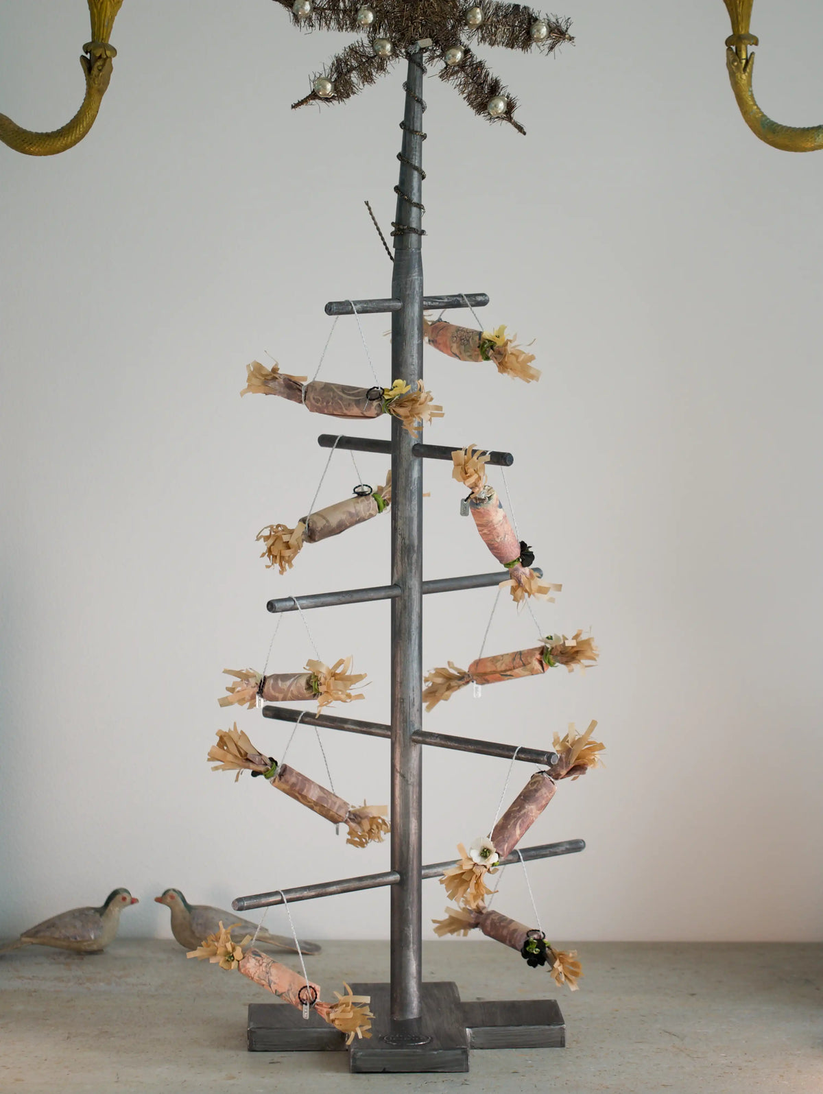 Decorative metal tree with branches and small paper crackers on a plain background