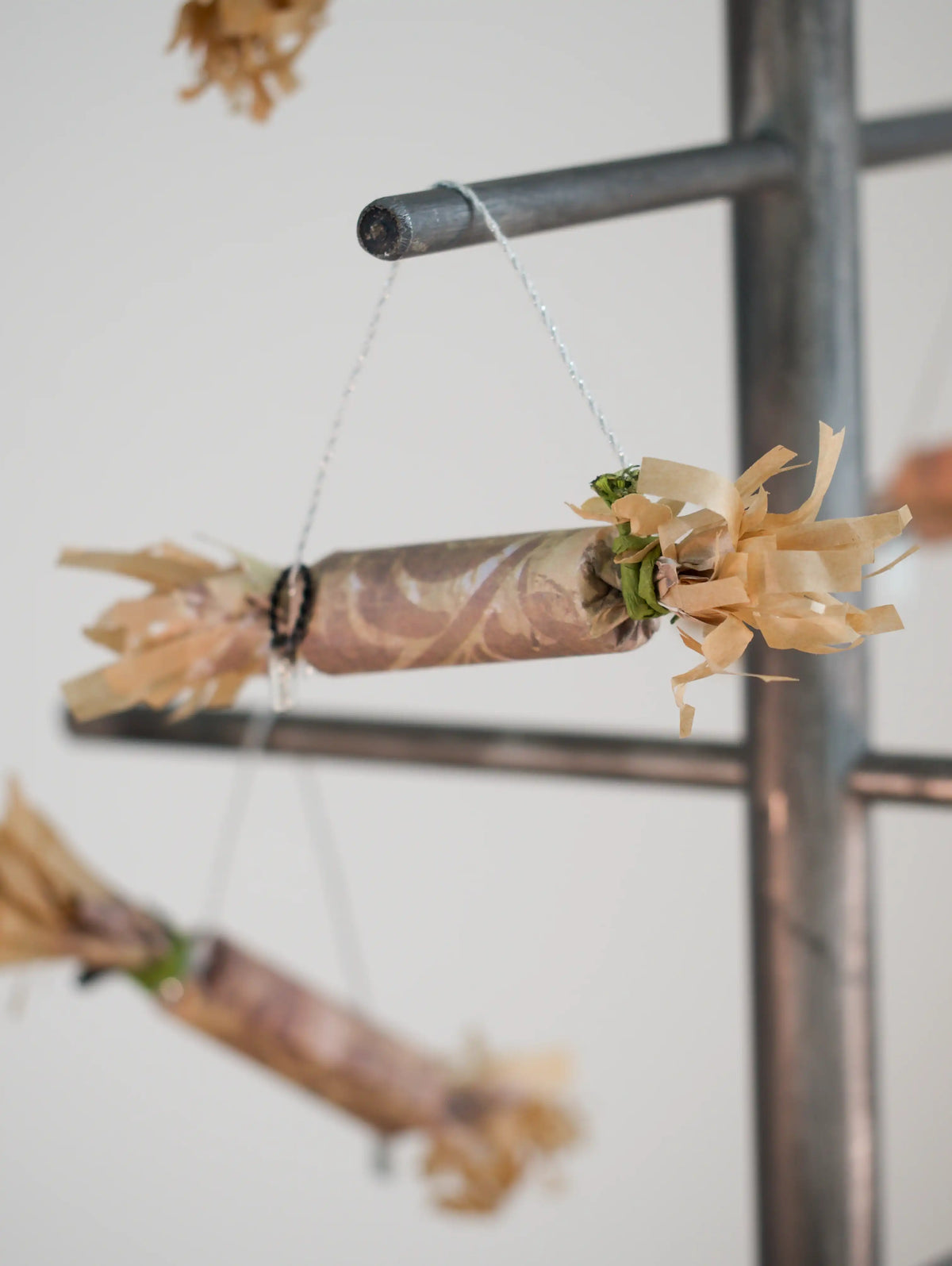 paper Christmas cracker with flower hanging on a rack against a white wall