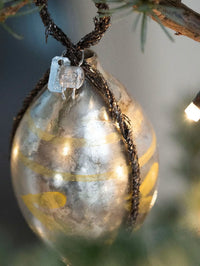 Decorative silver ornament with gold accents hanging on a tree branch.