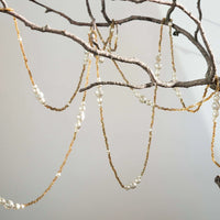 Garland with beads and amber brown chains hanging from a branch against a neutral background