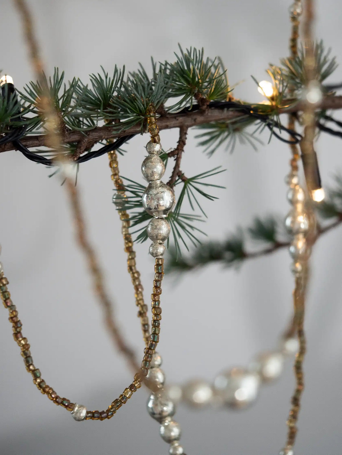 Decorative beaded strands hanging from a branch with small lights against a neutral background