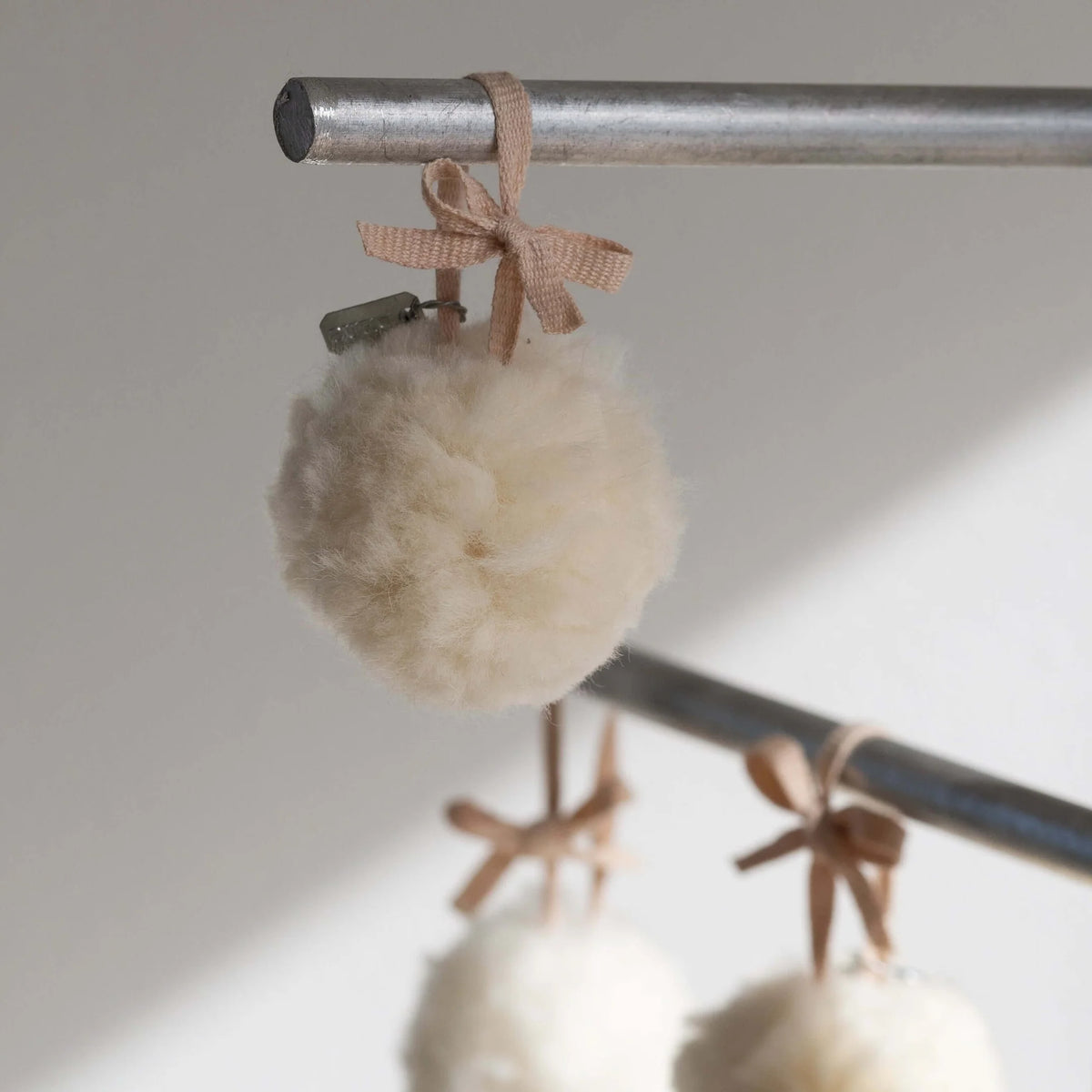 White pom-pom keychain with a pink bow attached to a metal rod on a neutral background