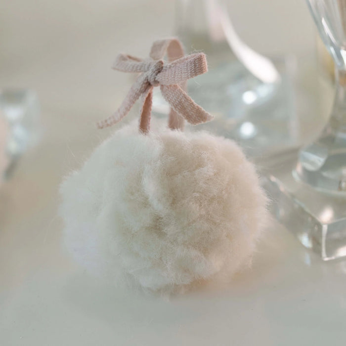 Fluffy white cotton ball with a pink bow on a neutral background