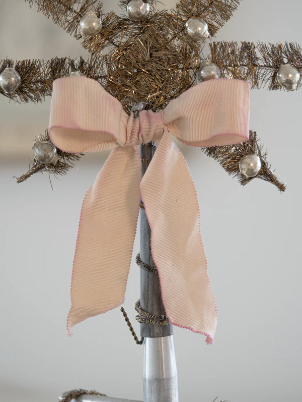 Pink bow on a Christmas tree with silver ornaments against a neutral background
