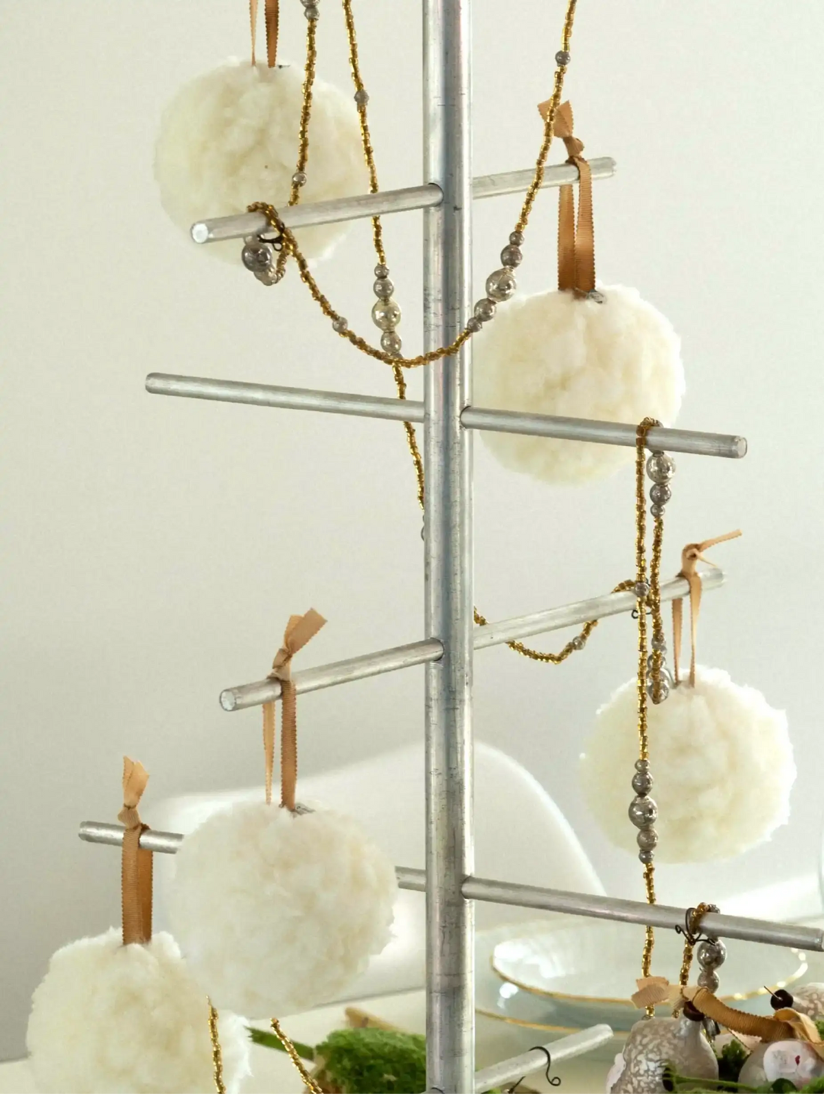 Decorative metal tree with white pom-pom ornaments and candles on a plain background