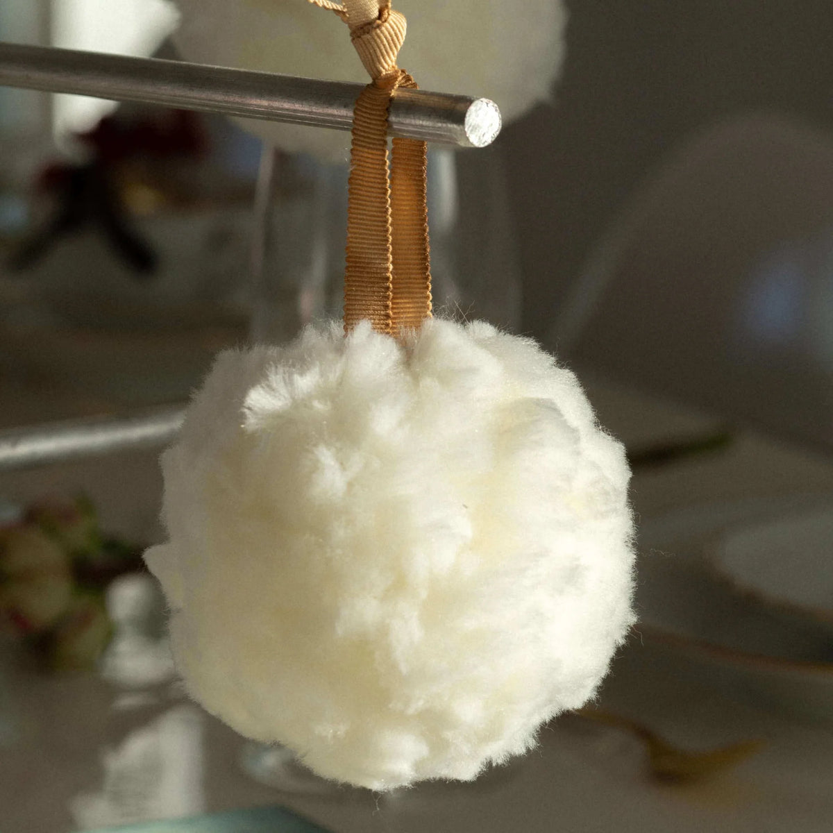 White fluffy pom-pom hanging from a gold ribbon on a blurred background