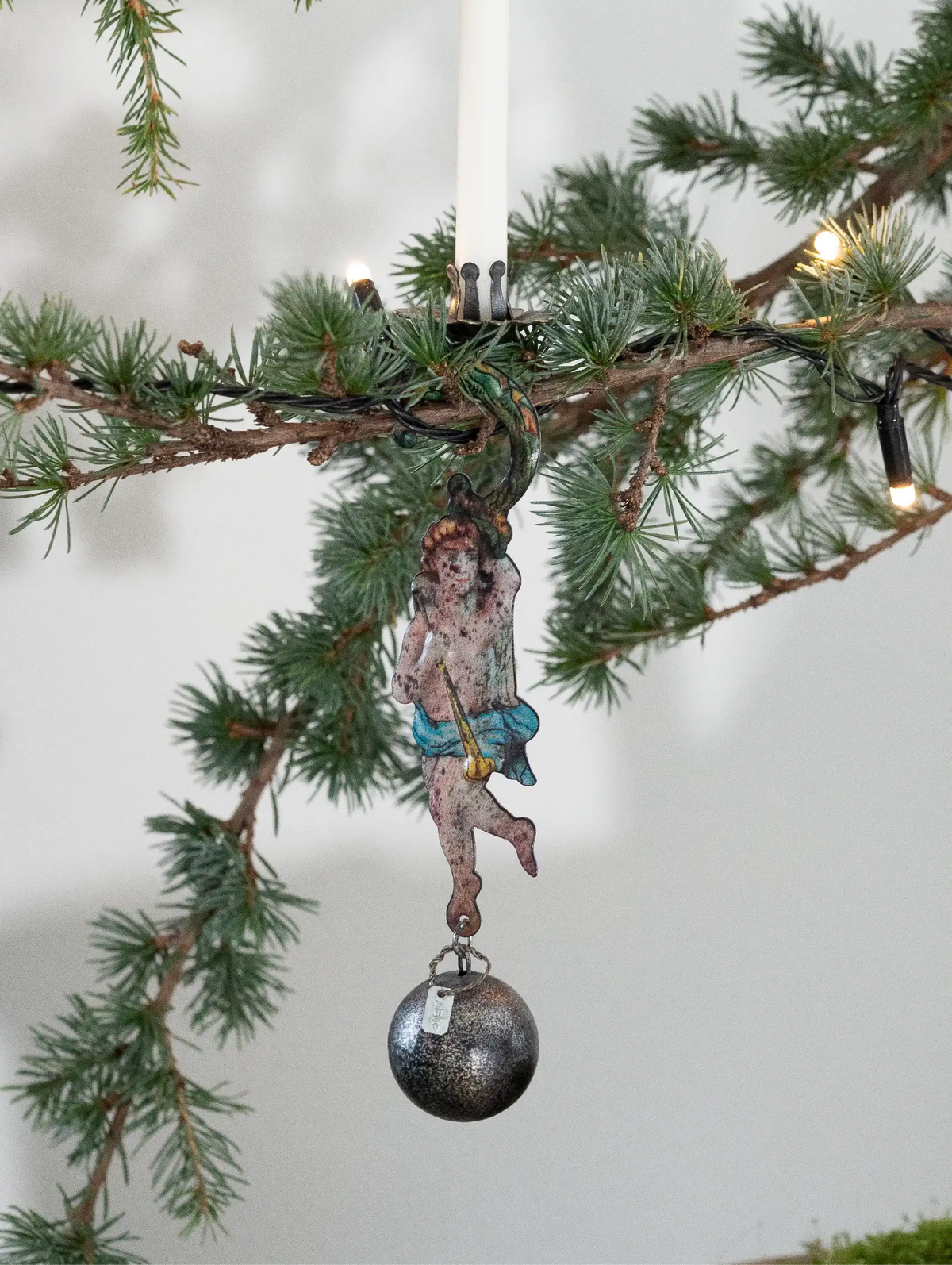 Decorative angel ornament with a silver ball hanging from a Christmas tree branch.