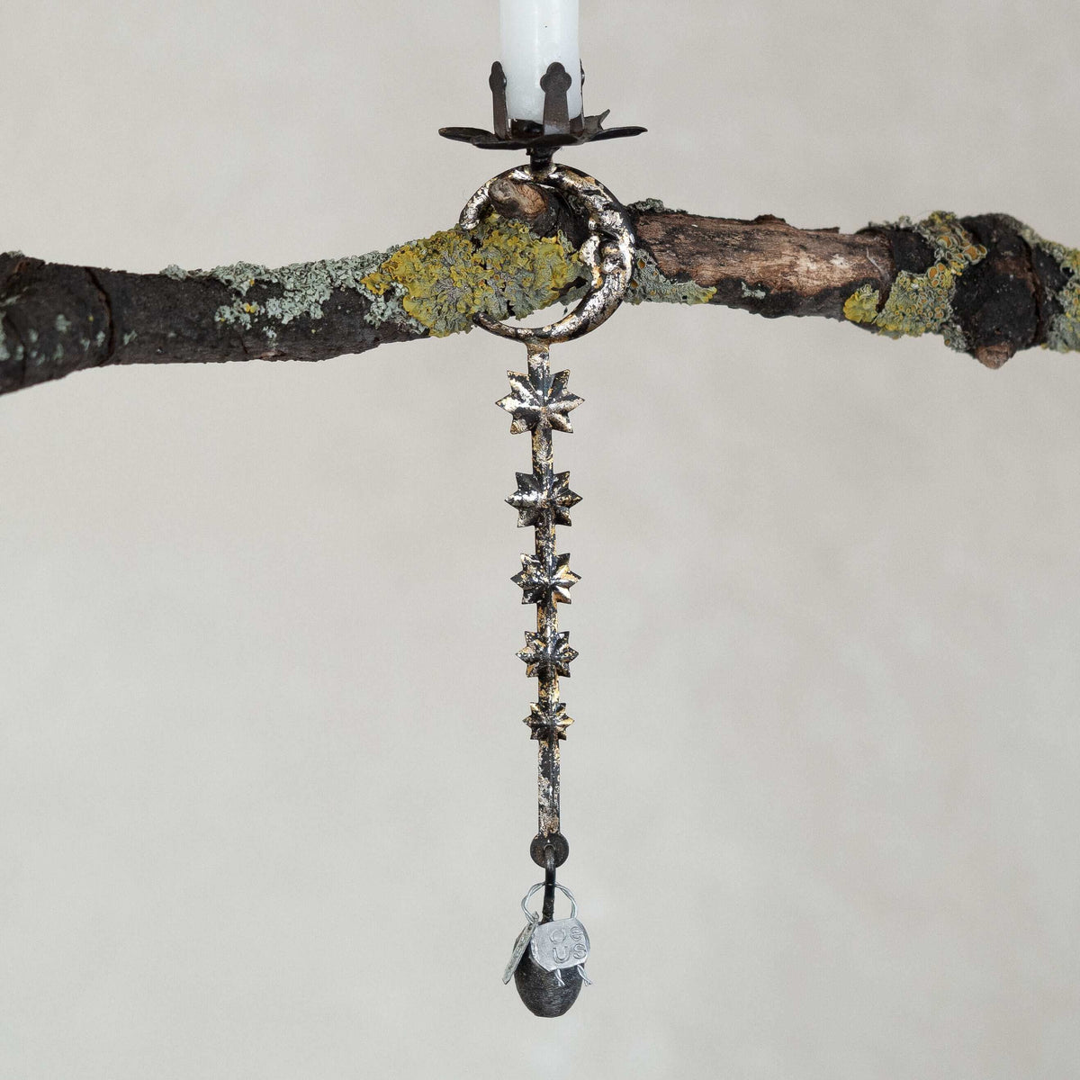 Decorative hanging candle holder with star-shaped design on a branch against a neutral background