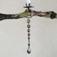 Decorative hanging candle holder with star-shaped design on a branch against a neutral background