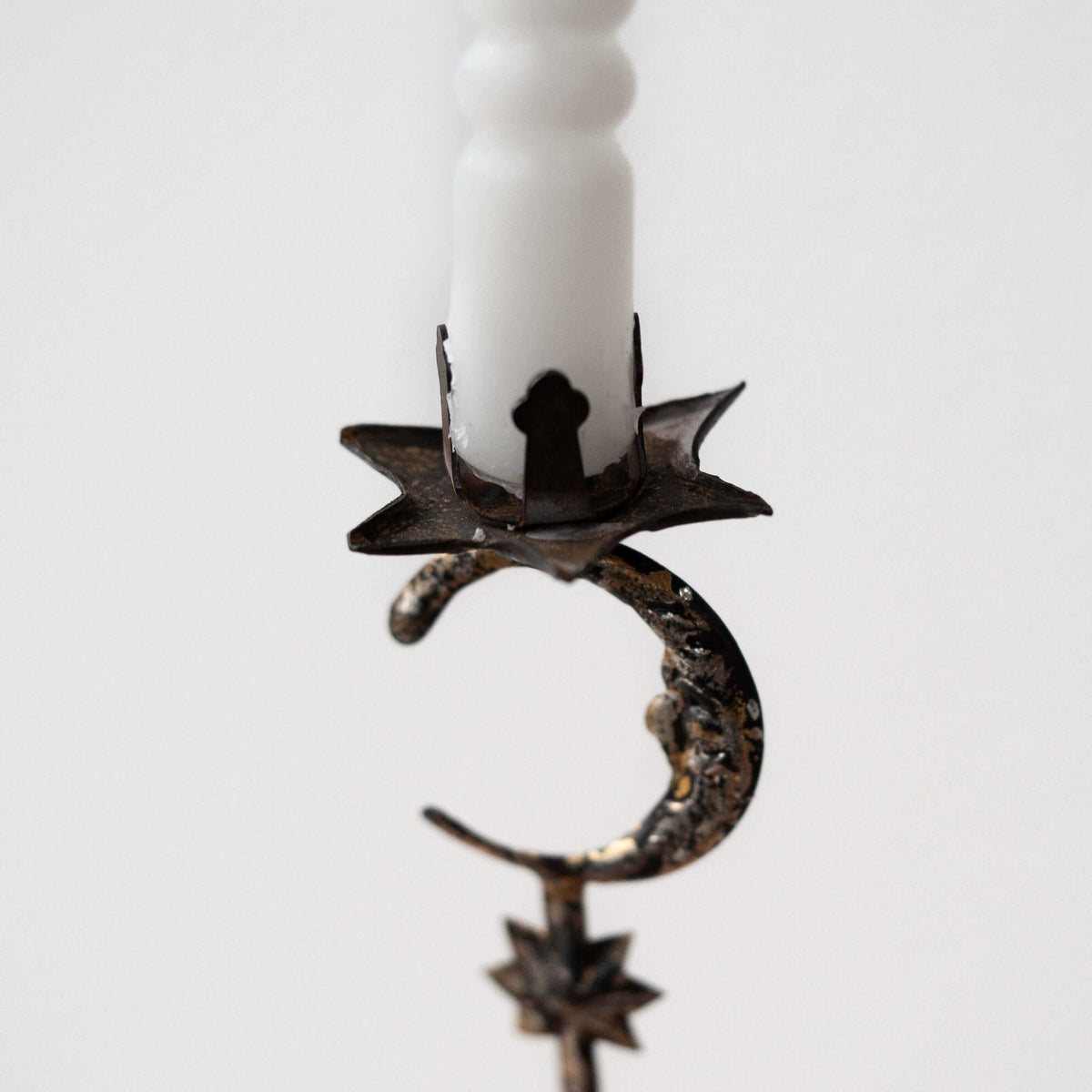 Decorative metal candle holder with star and moon design on a white candle against a light gray background