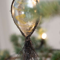 Close-up of a glass Christmas  bauble with tinsel , with a blurred background.