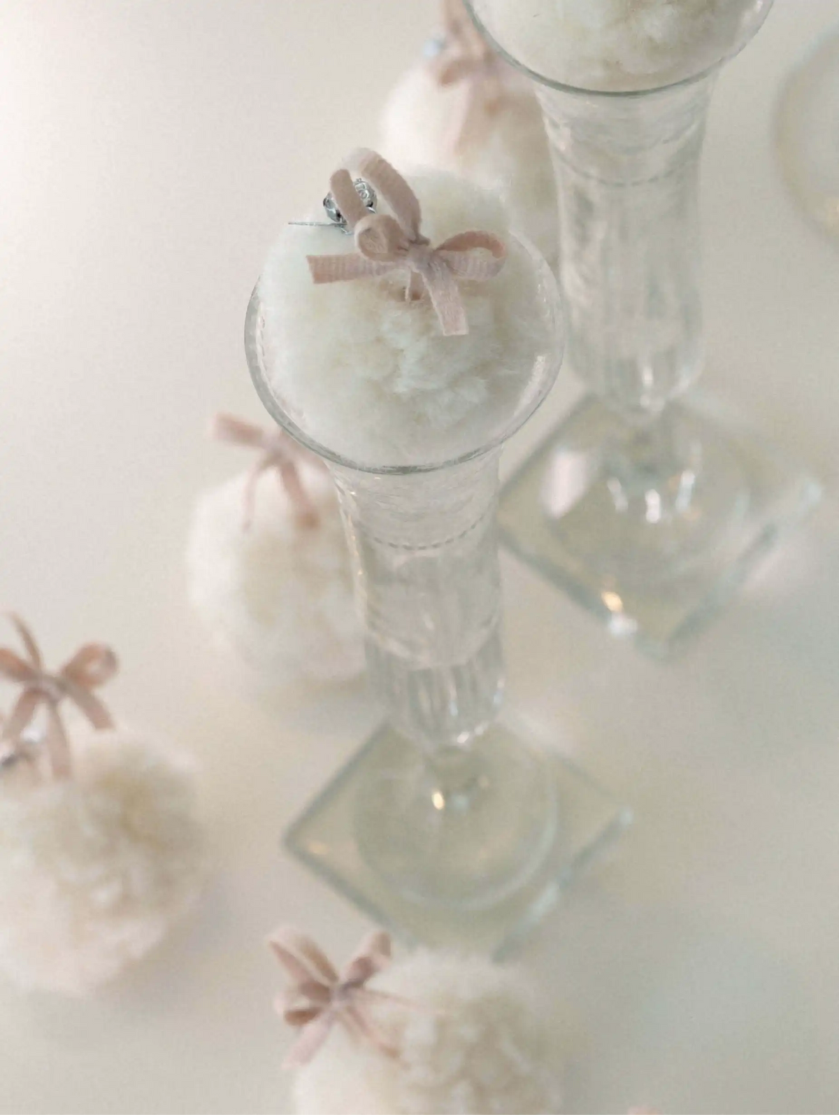 Clear glass candle holders with white wool snowball and pink ribbons on a white background