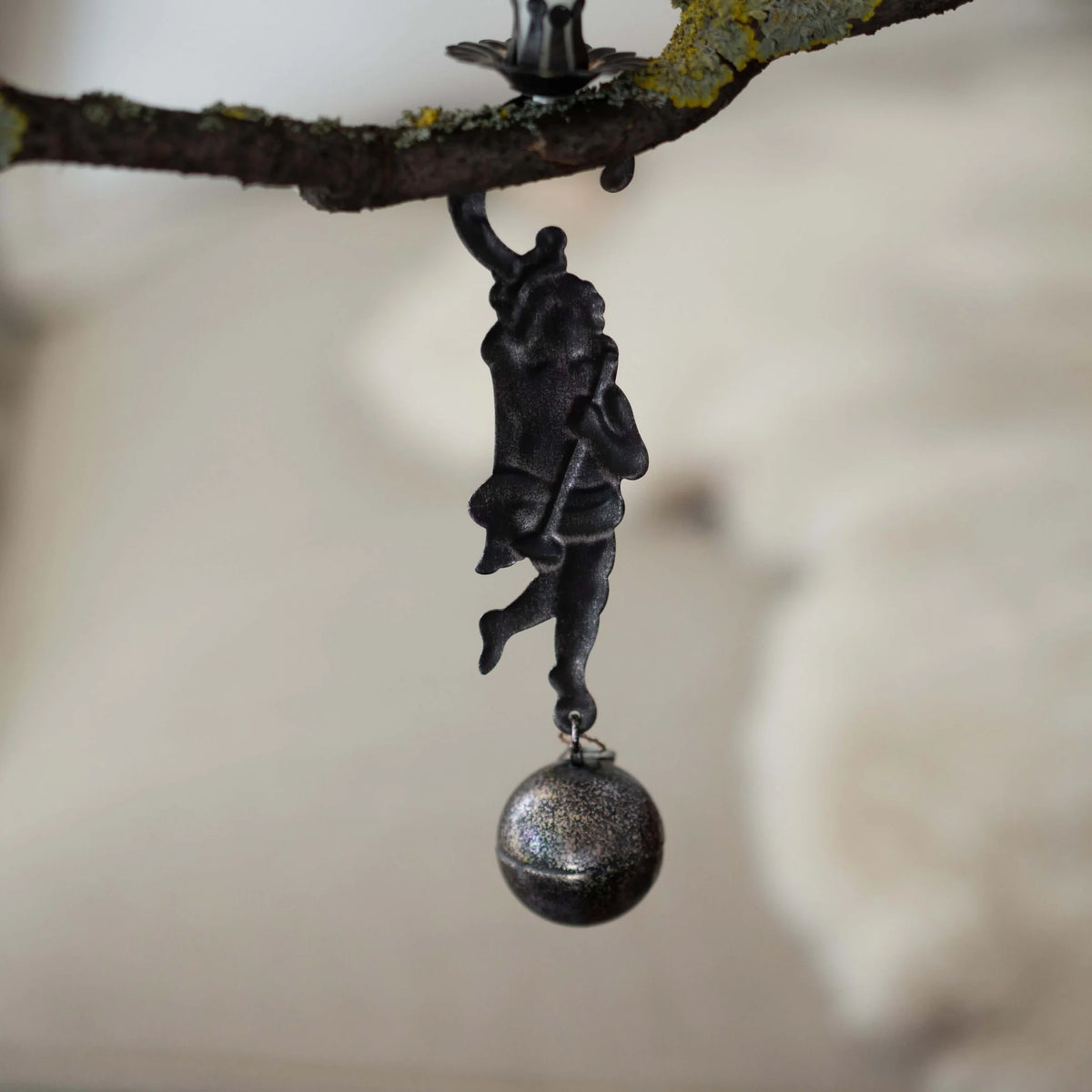 Decorative black figurine with a ball hanging from a branch against a blurred background