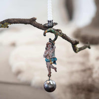 Decorative hanging figure with a ball on a branch against a blurred background