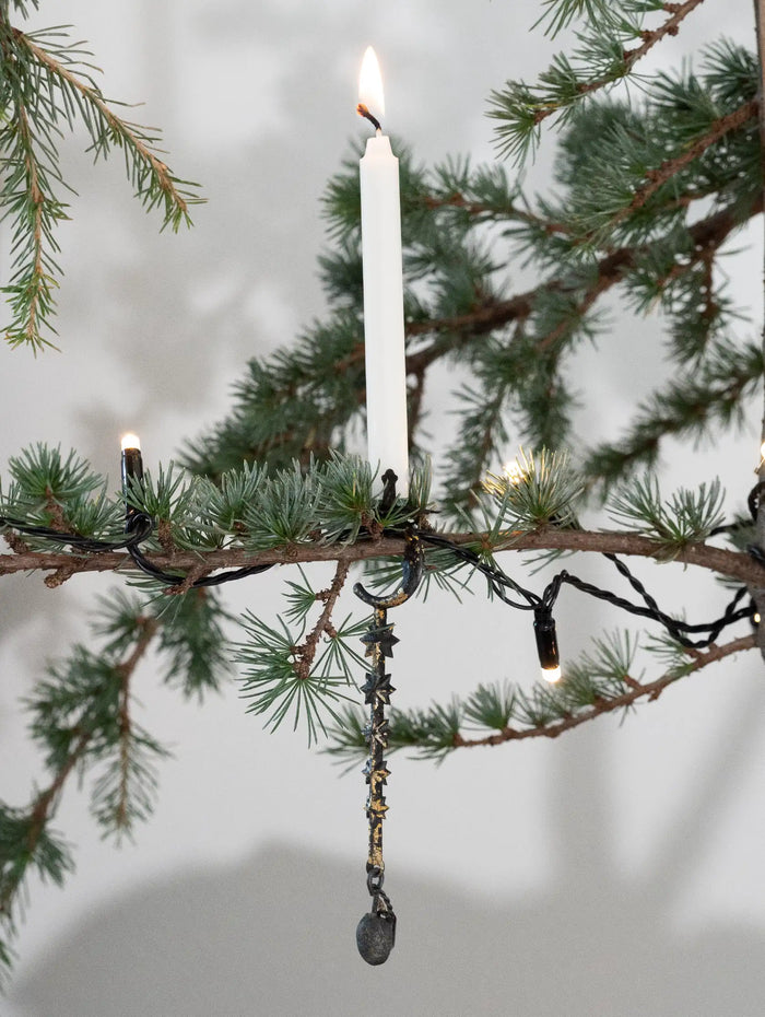 Decorative candle with hanging ornament on a branch against a blurred background