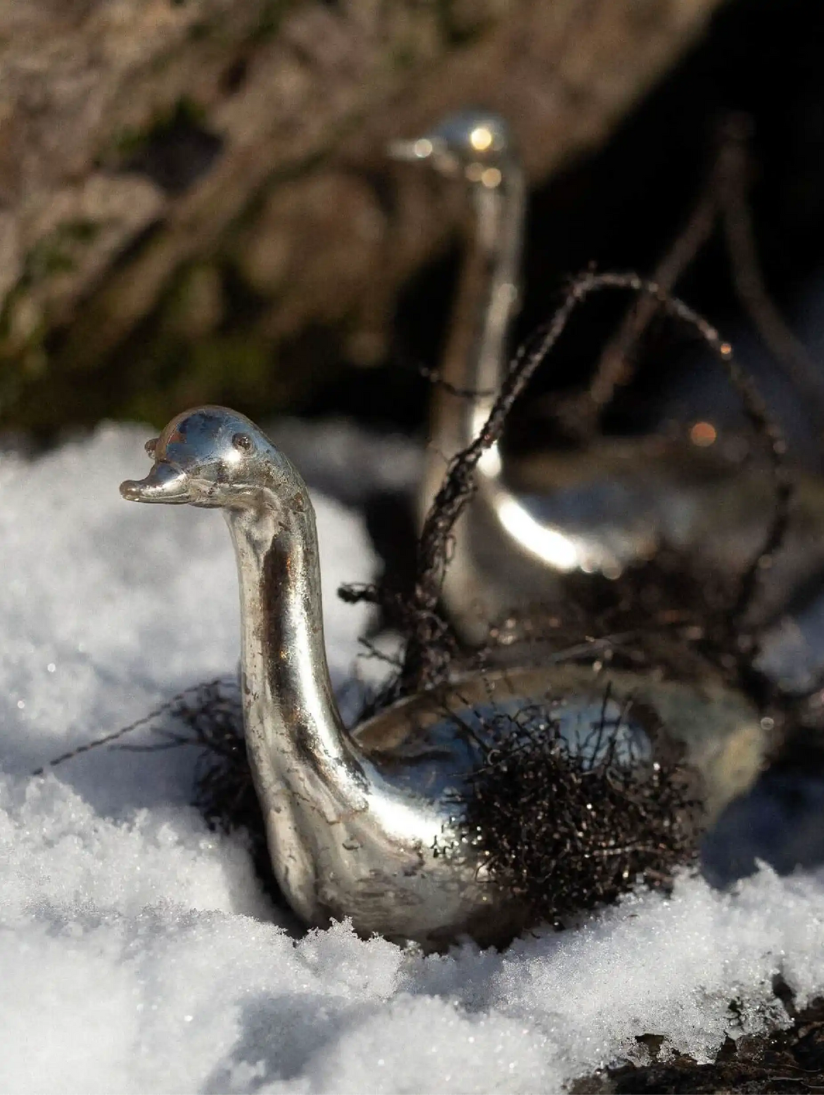 Metallic duck-shaped object in the snow with a blurred natural background