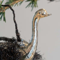 Metallic duck ornament on a branch with a neutral background