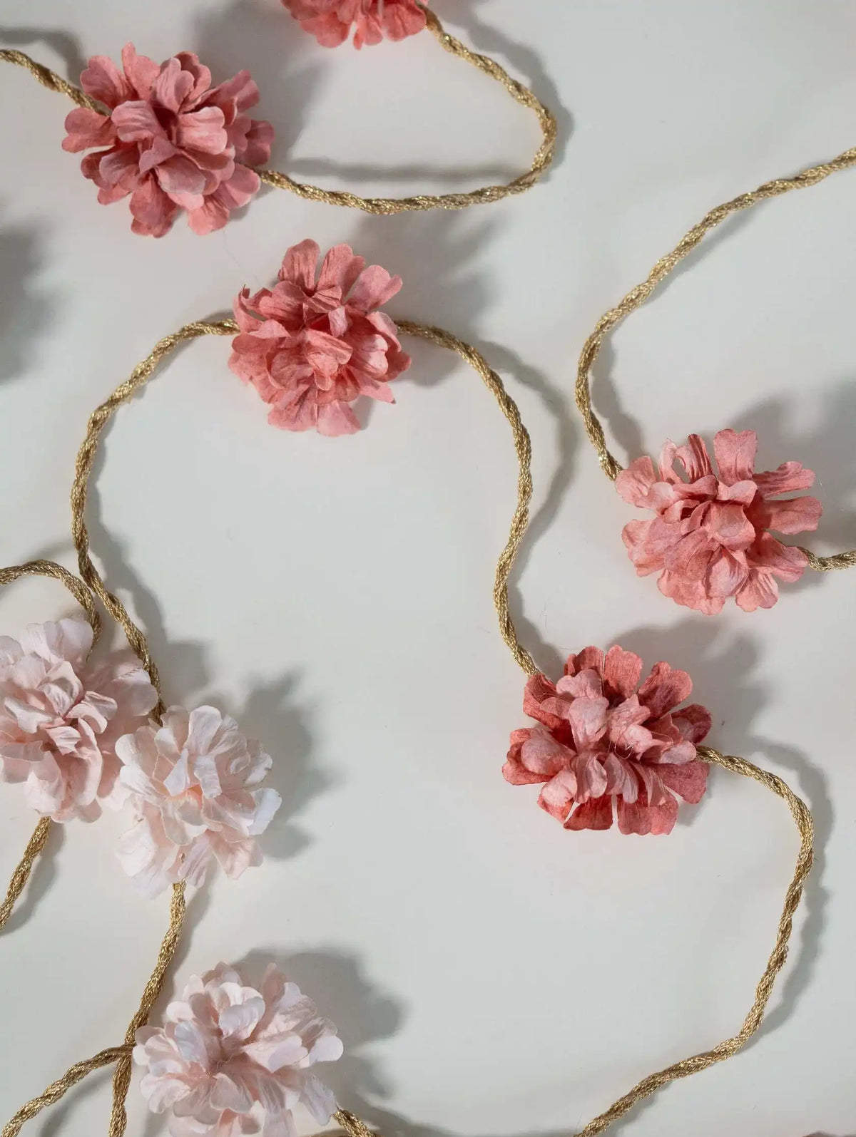 Floral garland with pink flowers and gold string on a white background