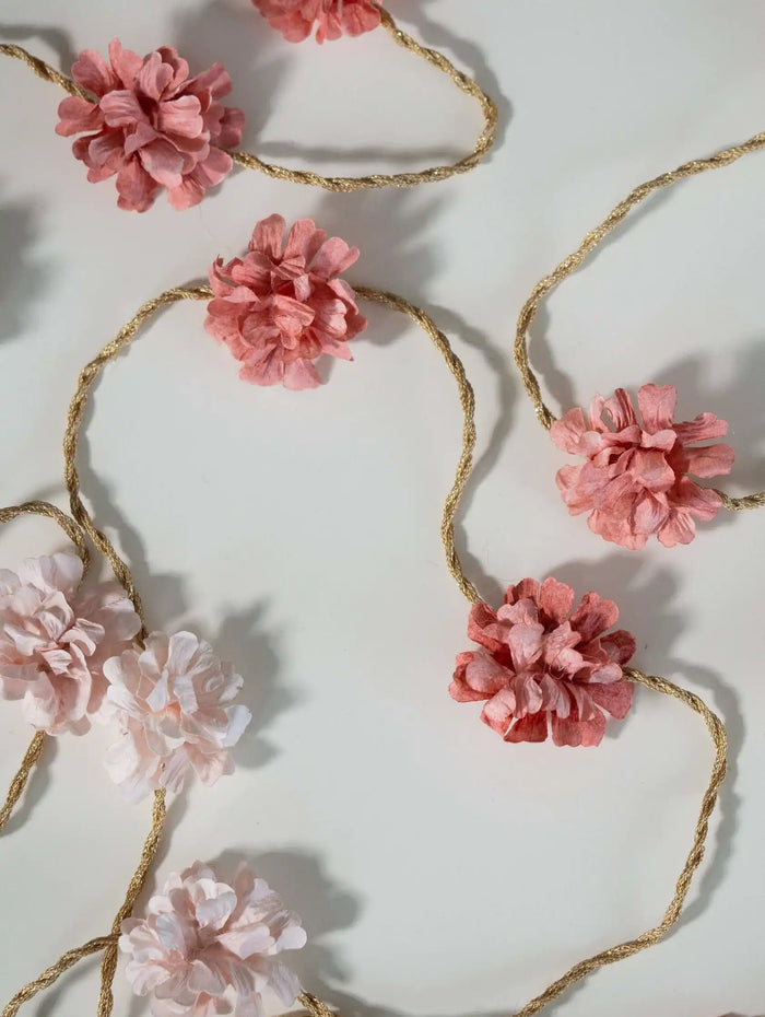 Floral garland with pink flowers and gold string on a white background