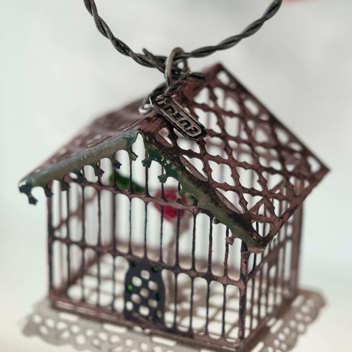 Bronze birdcage pendant on a black cord against a white background