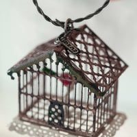 Bronze birdcage pendant on a black cord against a white background