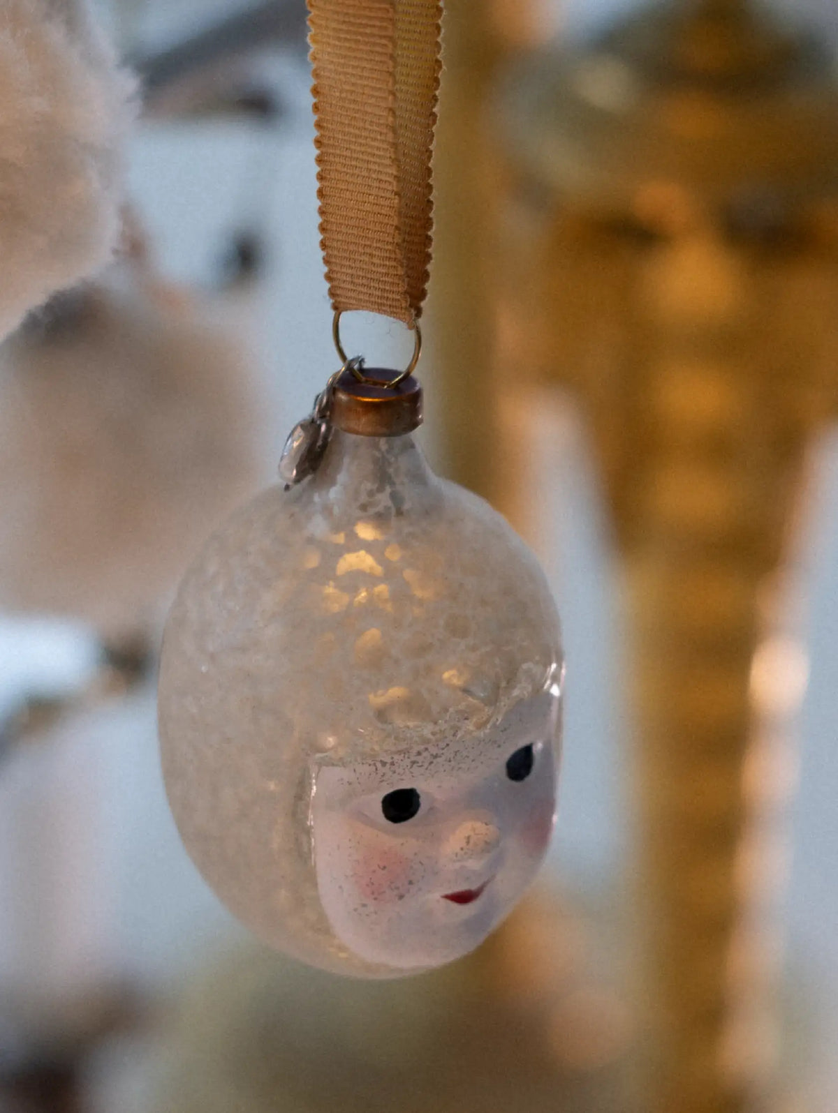 Decorative glass ornament with a face design hanging on a blurred background