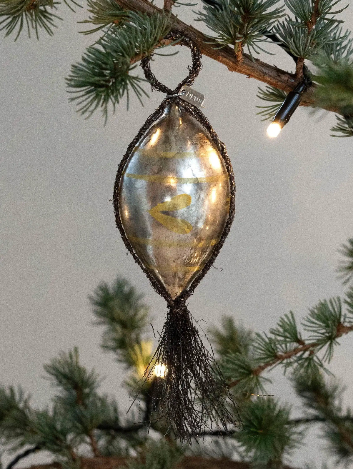 Decorative glass ornament with gold print hanging on a Christmas tree branch.