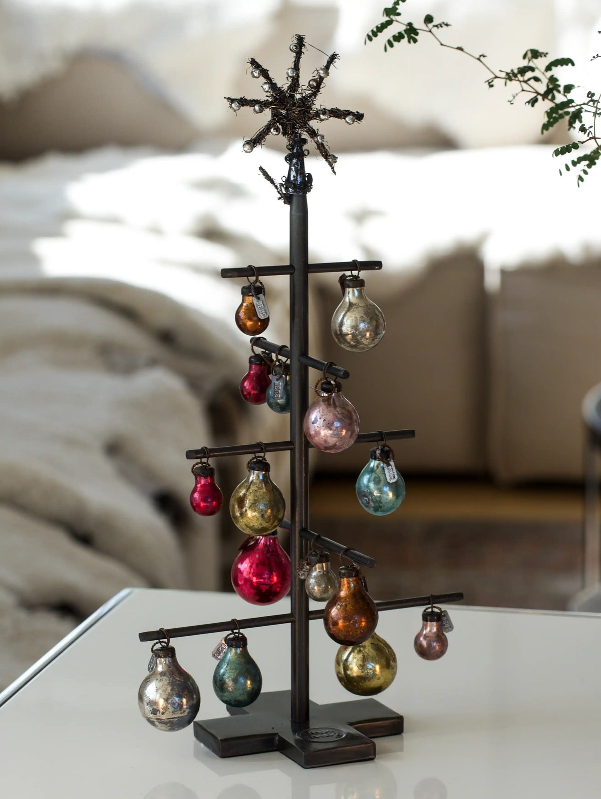 Decorative metal tree with colorful ornaments on a blurred indoor background
