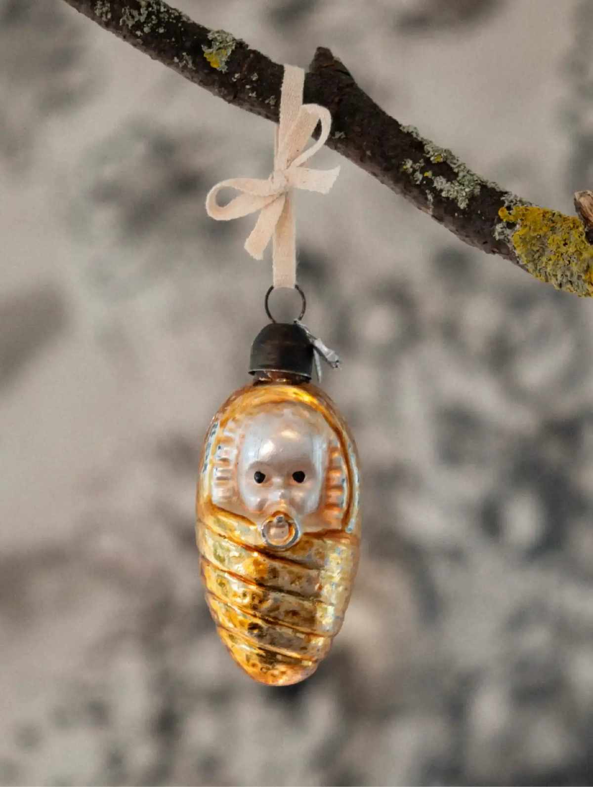 Decorative ornament shaped like a cocoon with a face, hanging on a branch.