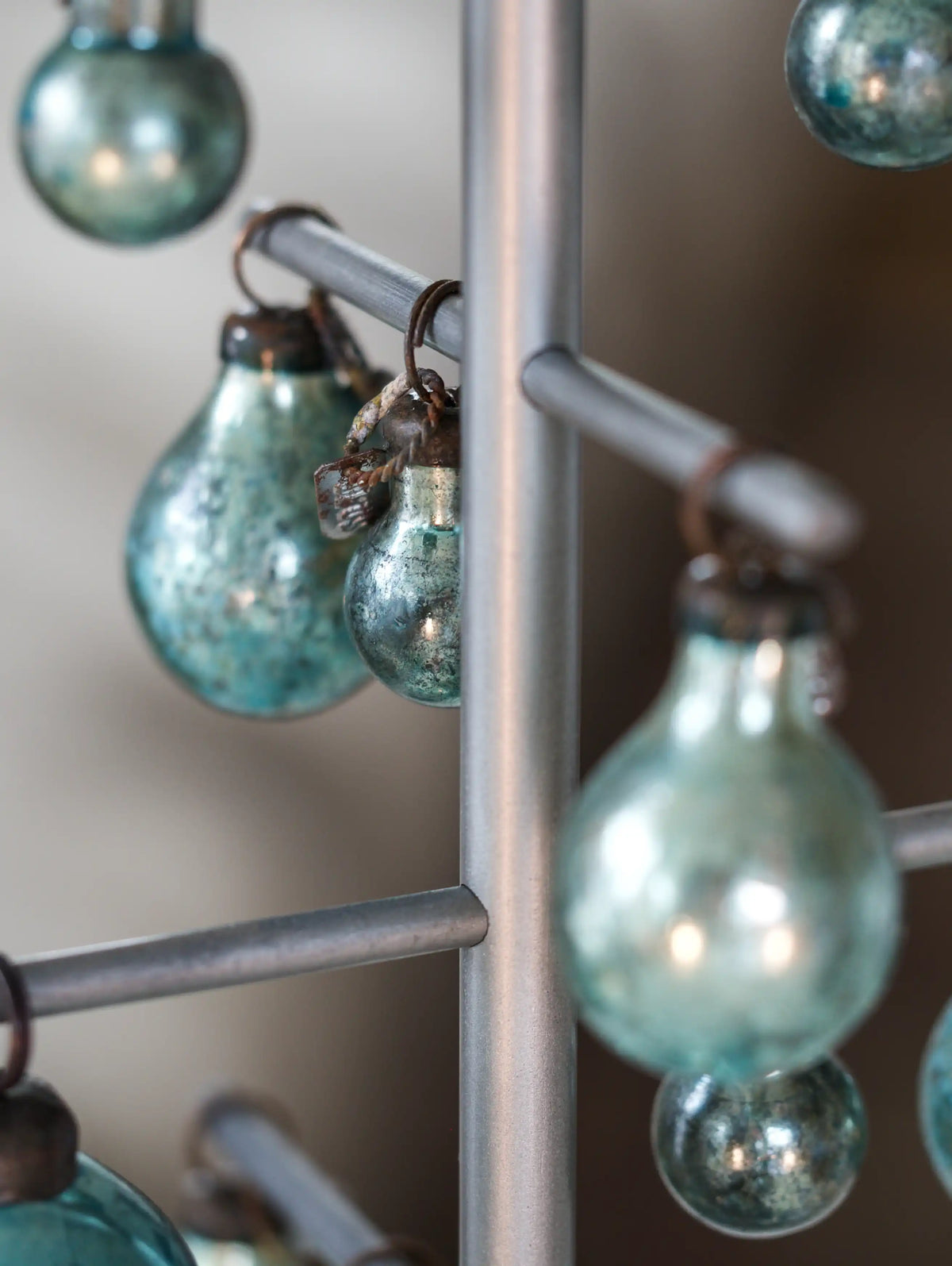 teal glass Christmas beads on a metal stand against a neutral background