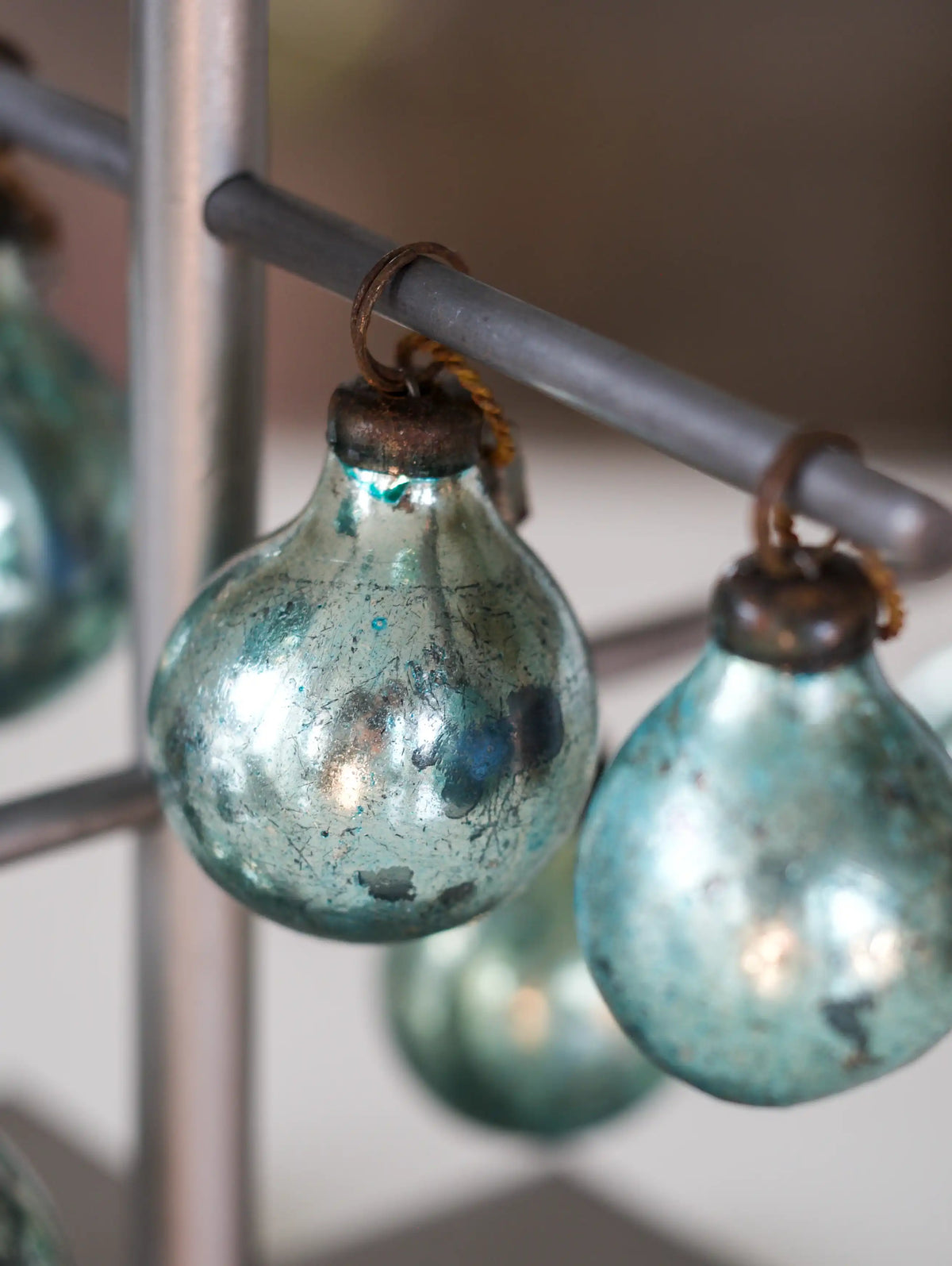 Vintage-style teal glass Christmas bulbs hanging from a metal rod.