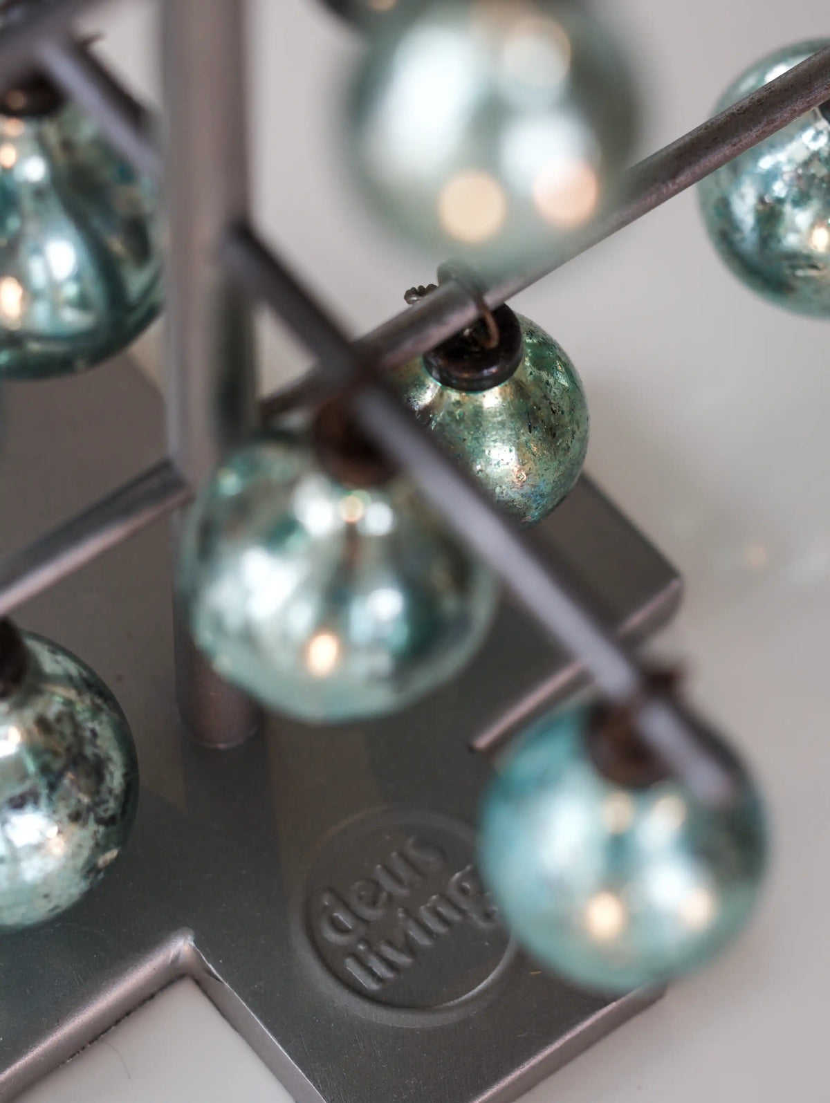 Close-up of a string of teal glass beads on a metal stand with Deus Living branding.