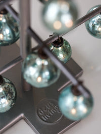 Close-up of a string of teal glass beads on a metal stand with Deus Living branding.