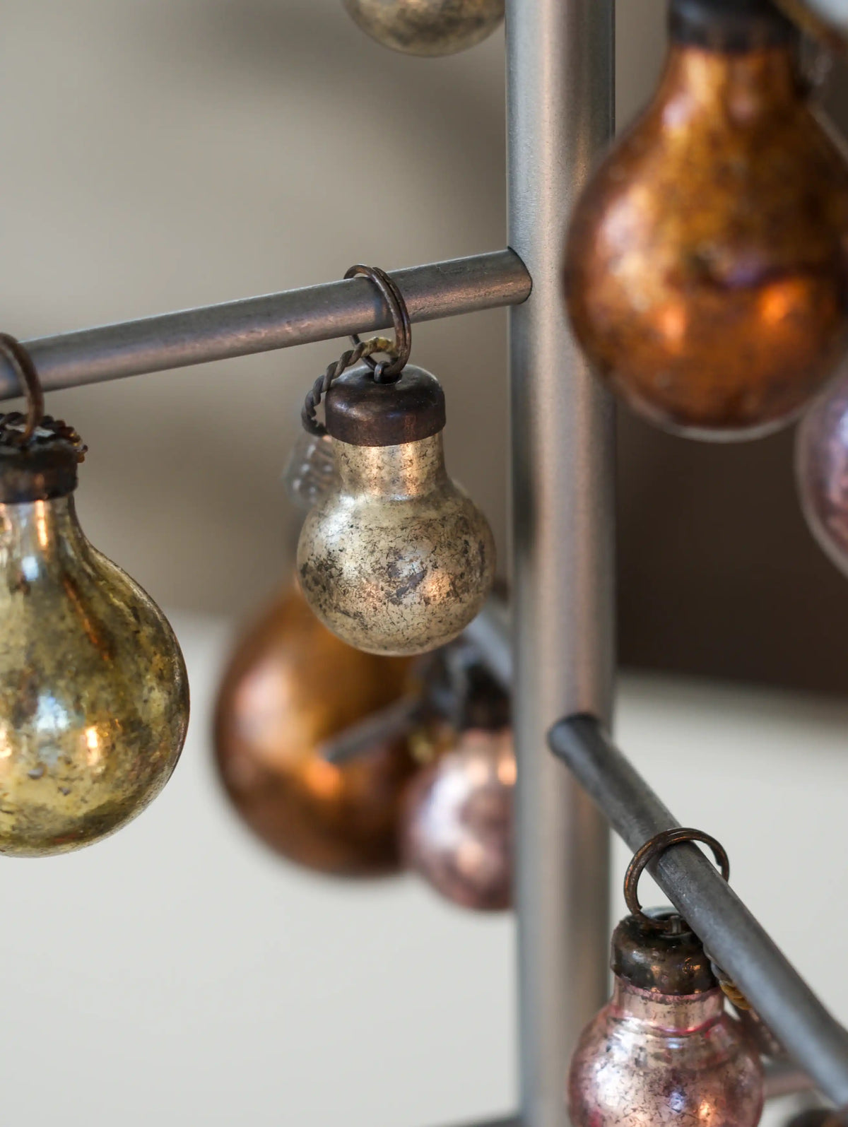Vintage-style Christmas bulbs hanging from a metal rod against a neutral background