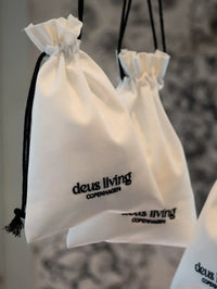 White drawstring bags with 'deus living Copenhagen' branding on a blurred background