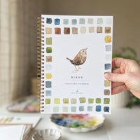 hand holding a water coloring book with a bird and colored blocks on cover