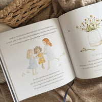 Open book with illustrations of three children and a vase of flowers, placed on a textured surface.