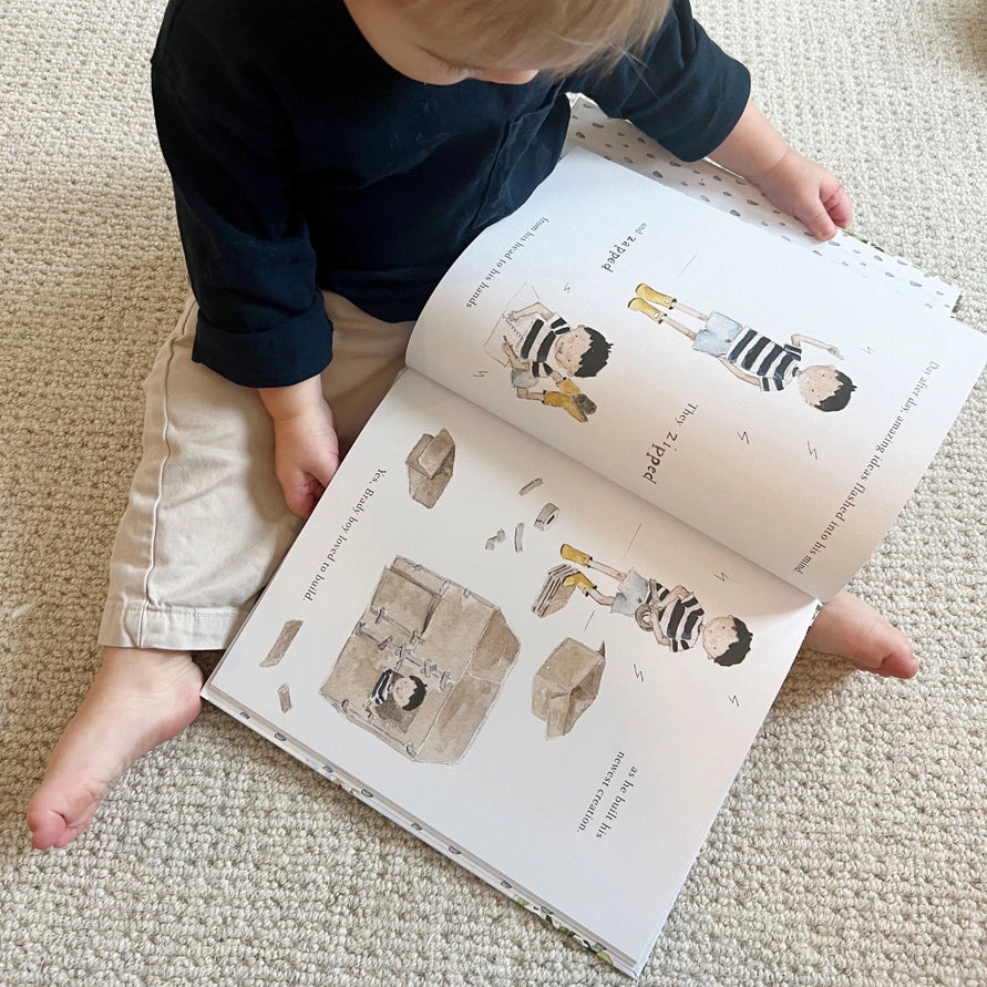 Child reading a book with illustrations of children playing on a carpeted floor.